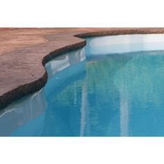 an empty swimming pool with blue water and stone edgings on the edge is seen in this photograph