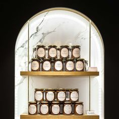 shelves with jars and labels on them in front of a marble wall, under a arched window