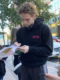 a young man standing on the sidewalk holding a piece of paper and looking at it