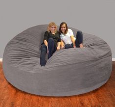 two women sitting on a bean bag chair in the middle of a hardwood floored room