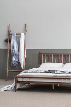 a wooden bed frame with white sheets and blankets on it, next to a gray wall