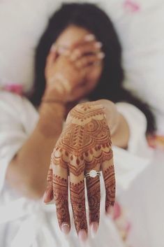 a woman laying in bed with her hand on her face and arm covered by henna