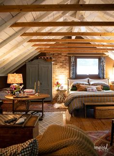 an attic bedroom with exposed wood beams and brick walls, bed in foreground, couch on far side