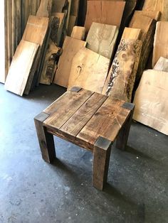 a table made out of wood sitting in front of stacks of wooden planks on the floor