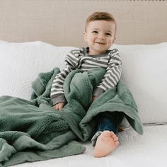 a little boy sitting on top of a bed under a blanket