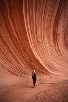 a woman is standing in the middle of a large wave like area with sand on it