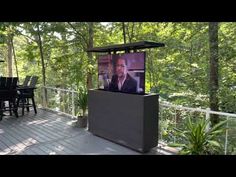 a television on top of a wooden table in the middle of a deck surrounded by trees