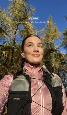 a woman in pink jacket standing next to trees with ear buds on her ears and headphones