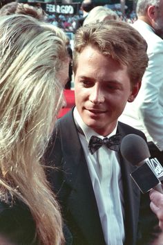 a man in a tuxedo talking to someone on the red carpet at an event