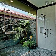 a walk in shower sitting inside of a bathroom next to a lush green plant and stone wall