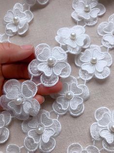 a hand is holding some white flowers on a tablecloth with pearls in the middle