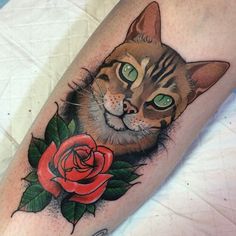 a cat with green eyes and a rose tattoo on its leg, sitting next to a white sheet