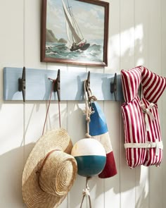 three hats hanging from hooks on a wall next to a hat rack with two buoys