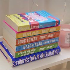 a stack of books sitting on top of a table next to a pink cup and candle