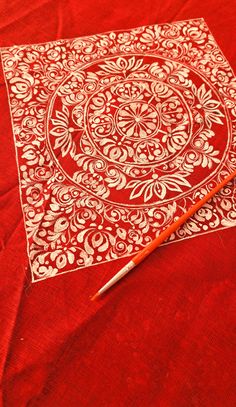 a red table cloth with white designs on it and an orange pen laying next to it