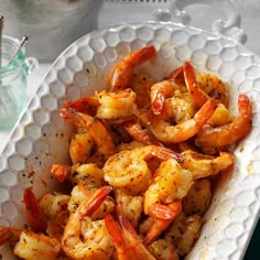 a white bowl filled with cooked shrimp and garnished with seasoning next to utensils