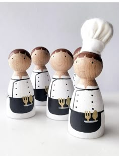 three wooden dolls are dressed in black and white outfits with a chef's hat on their head