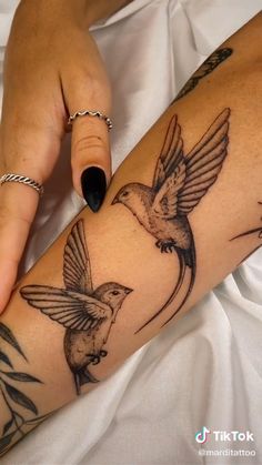 a woman's arm with two birds on it and one bird flying towards the other