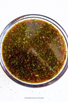 a glass bowl filled with green sauce on top of a white counter