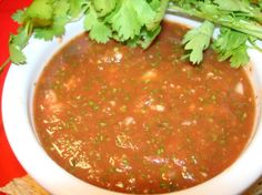 a white bowl filled with chili and cilantro on top of a red table