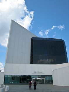 two people are standing in front of a large white building with a black glass window