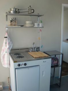 a small kitchen with an oven, sink and shelf above the stove is also used as a shelving unit