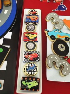 decorated cookies are sitting on trays next to race cars and other toys at a birthday party