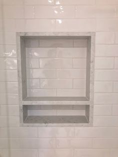 a bathroom with white tile and shelves in the wall