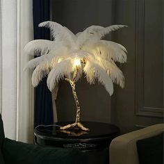 a white palm tree lamp sitting on top of a table next to a chair and window