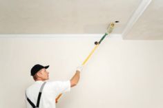 a man in white shirt and black pants painting a ceiling with paint rollers on it