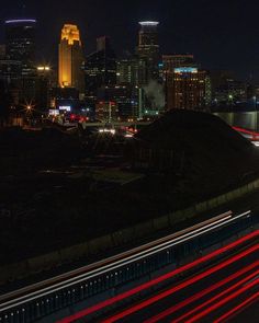 the city skyline is lit up at night with red and white light streaks in the foreground