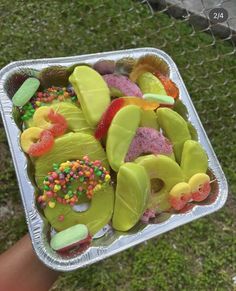 a person holding up a tin foil container filled with different colored candies and donuts