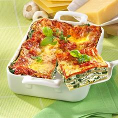 a casserole dish with spinach, cheese and sauce in it on a green tablecloth