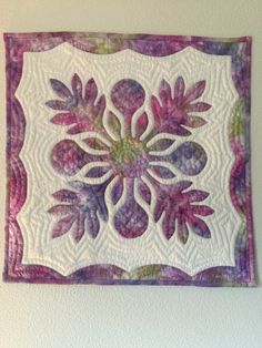 a white wall hanging with a purple and green quilted design on it's side