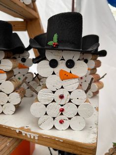 three snowmen made out of wood sticks and wearing black hats, standing on top of a table