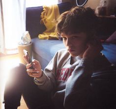 a young man sitting on the floor holding a cell phone to his ear and looking at it