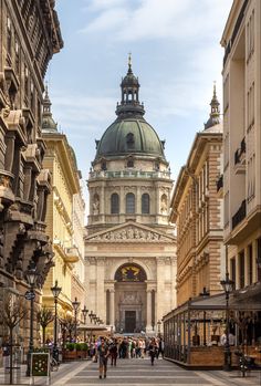 people are walking down the street in front of an old building with a dome on top