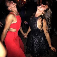 two women in red and black dresses holding hands while standing next to each other at a party