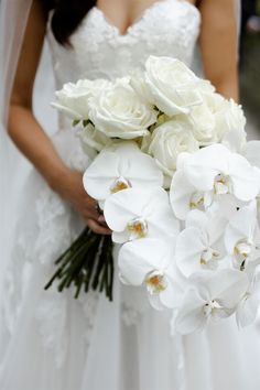 a bride holding a bouquet of white orchids and roses in her wedding day dress