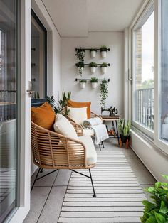 a balcony with potted plants and wicker furniture on the floor next to large windows