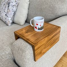 a wooden table with a coffee cup on it in front of a couch and pillows