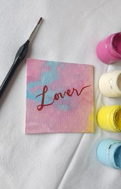 some paint bottles are sitting next to a canvas with the word love painted on it