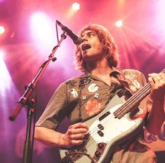 a man holding a guitar while standing in front of a microphone on top of a stage