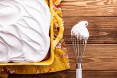 a whisk is next to a yellow dish with white icing on it