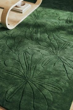 a green rug with an intricate design on the floor next to a chair and remote control