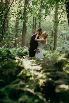 a bride and groom are kissing in the woods on their wedding day, surrounded by greenery