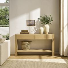 a table with two vases on it in front of a window and a couch