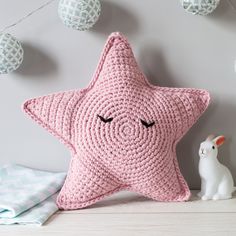 a pink crocheted star pillow sitting on top of a table next to a white bunny