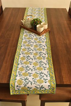 a wooden table topped with a green and yellow runner next to a potted plant