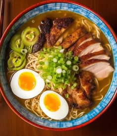 a bowl of ramen with meat, eggs and scallions in it on a wooden table